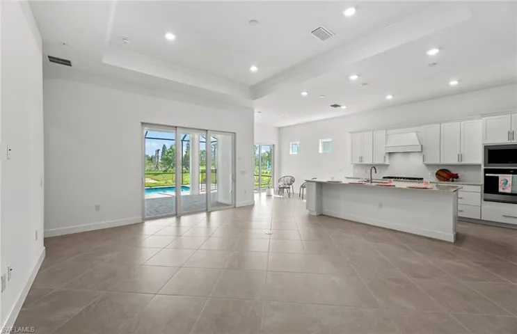 Kitchen featuring custom range hood, a center island with sink, a raised ceiling, appliances with stainless steel finishes, and light tile floors