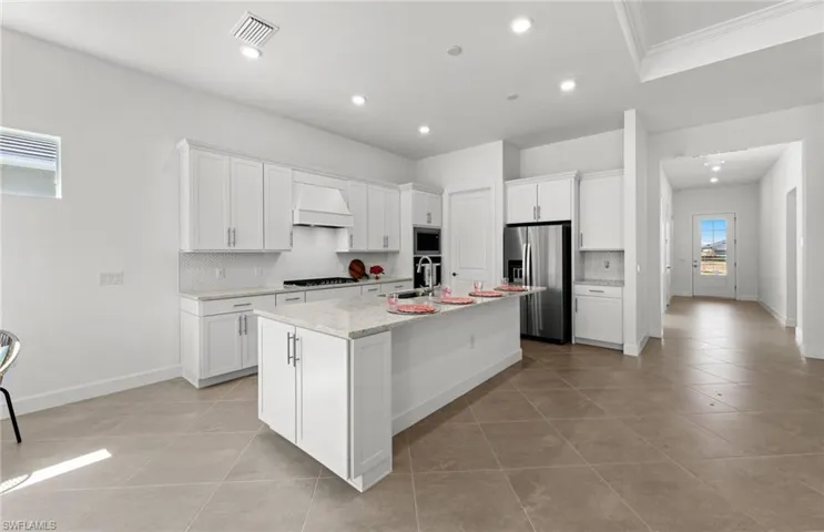 Kitchen with tasteful backsplash, light tile flooring, premium range hood, a kitchen island with sink, and appliances with stainless steel finishes
