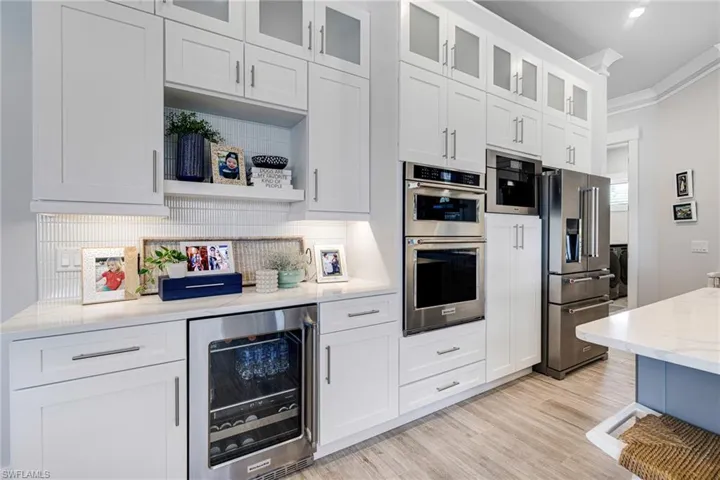 Kitchen featuring wine cooler, white cabinets, ornamental molding, appliances with stainless steel finishes, Miele coffee maker, and glass insert cabinets