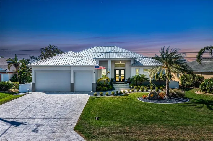 View of front of home with paver driveway, stucco siding, metal roof, 3 car garage, and custom front lawn