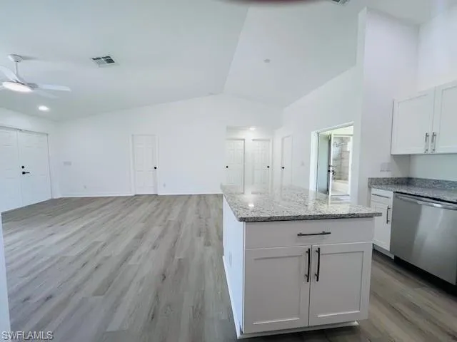 Kitchen with light stone counters, dishwasher, light wood finished floors, open floor plan, and white cabinets