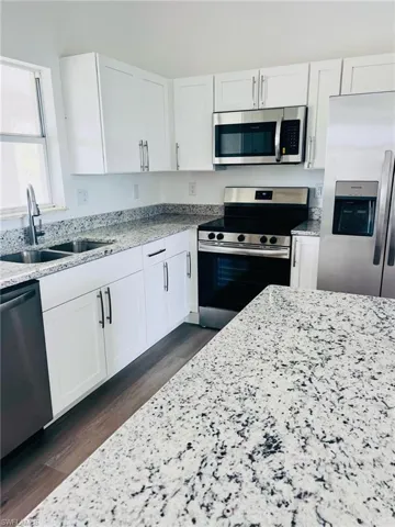 Kitchen featuring appliances with stainless steel finishes, white cabinets, and light stone counters