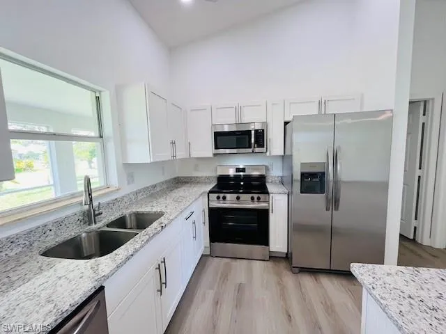 Kitchen with appliances with stainless steel finishes, light stone countertops, white cabinets, and a towering ceiling