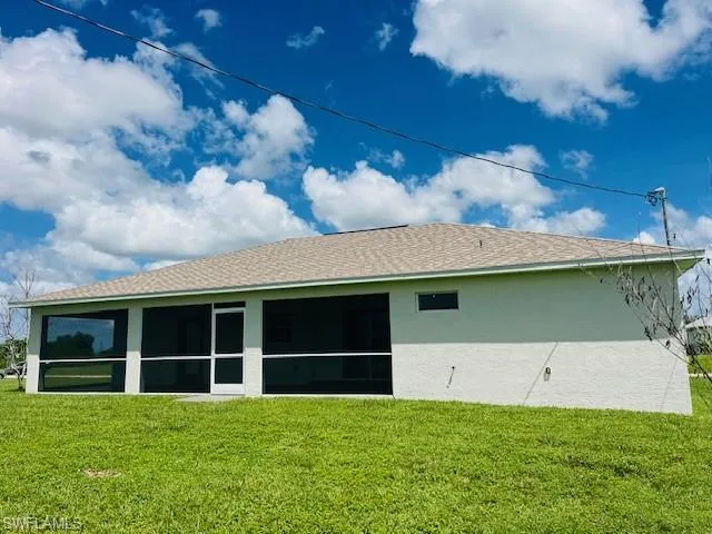 Back of house with a lawn, roof with shingles, stucco siding, and a sunroom