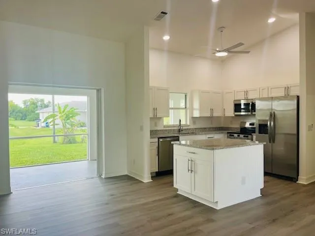 Kitchen featuring a high ceiling, stainless steel appliances, a ceiling fan, light stone counters, and dark wood finished floors