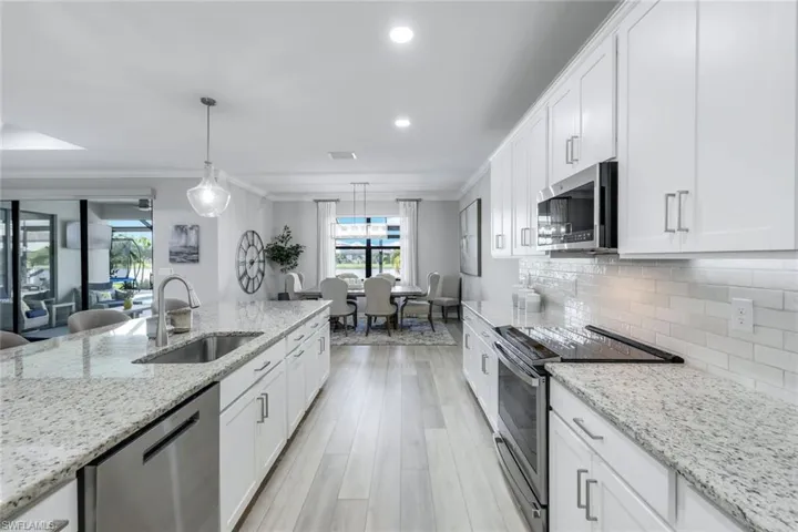 Kitchen featuring white cabinetry, appliances with stainless steel finishes, hanging light fixtures, and sink