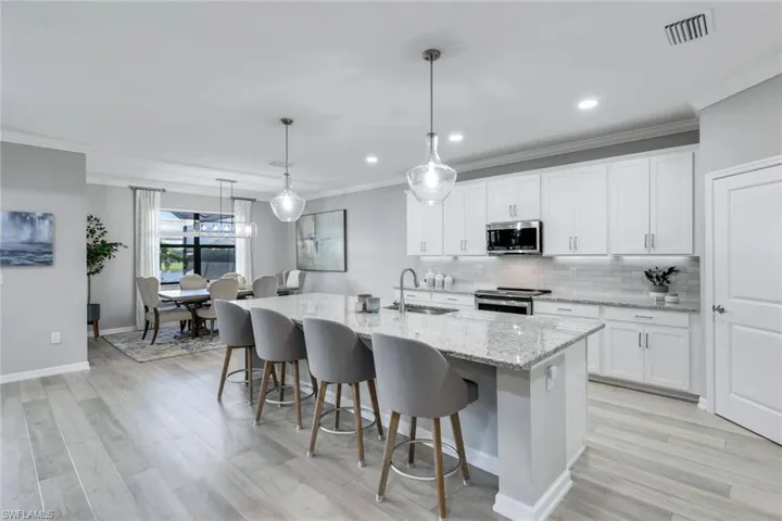 Kitchen with sink, white cabinets, stainless steel appliances, a center island with sink, and decorative light fixtures