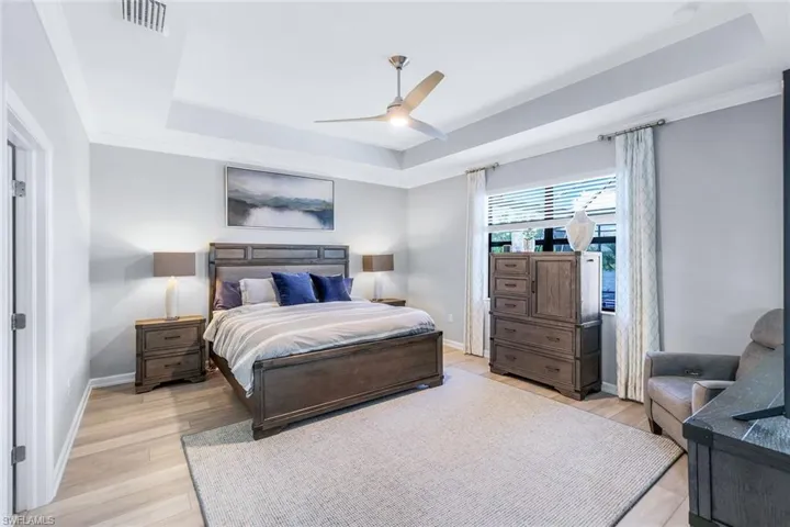 Bedroom with a raised ceiling, light hardwood / wood-style floors, crown molding, and ceiling fan