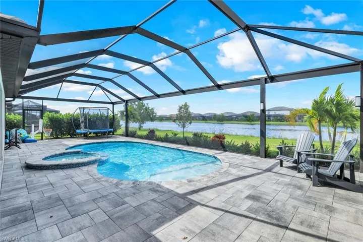 View of pool with a water view, an in ground hot tub, a patio area, and glass enclosure