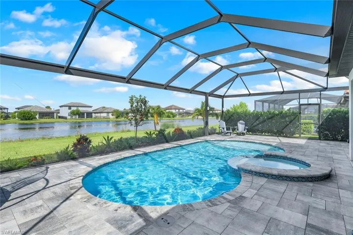 View of swimming pool featuring an in ground hot tub, a patio, glass enclosure, and a water view