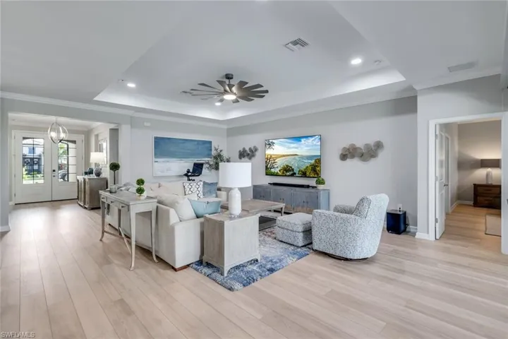 Living room with ceiling fan with notable chandelier, light hardwood / wood-style flooring, crown molding, and a raised ceiling