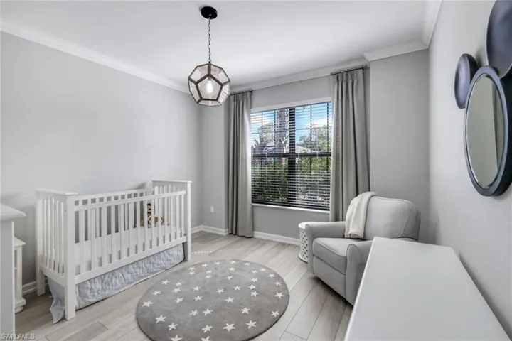 Bedroom with a crib, light hardwood / wood-style floors, and ornamental molding