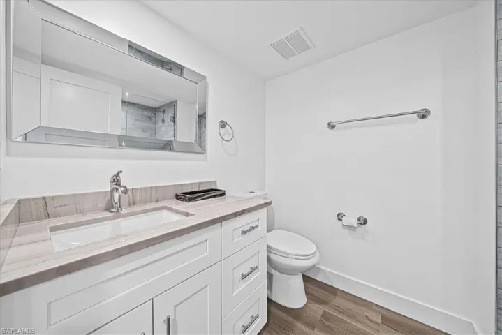 Full bath featuring a tile shower, vanity, and dark wood-type flooring
