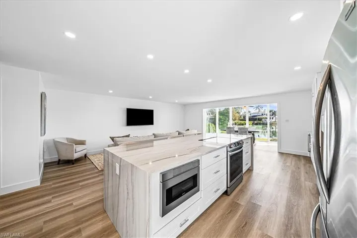 Kitchen with open floor plan, stainless steel appliances, light stone counters, white cabinets, and recessed lighting