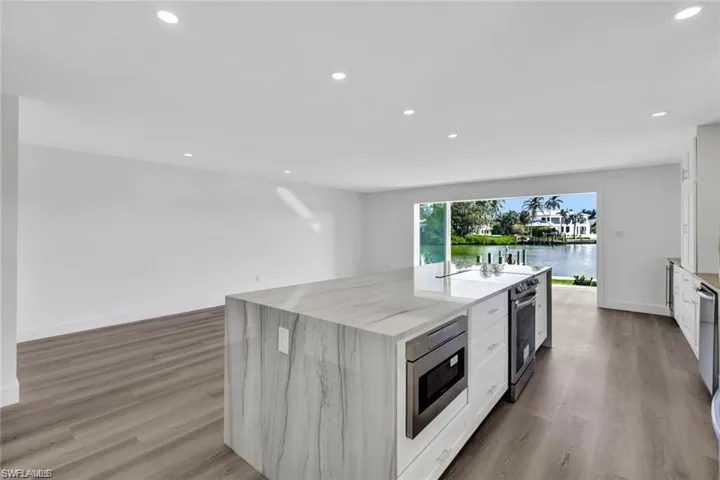 Kitchen with white cabinets, light wood-type flooring, light stone countertops, recessed lighting, and stainless steel appliances