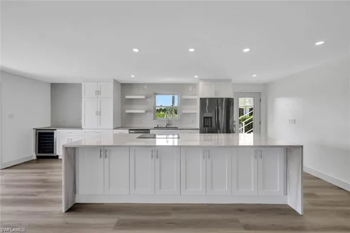 Kitchen with white cabinets, backsplash, light stone countertops, stainless steel fridge, and beverage cooler