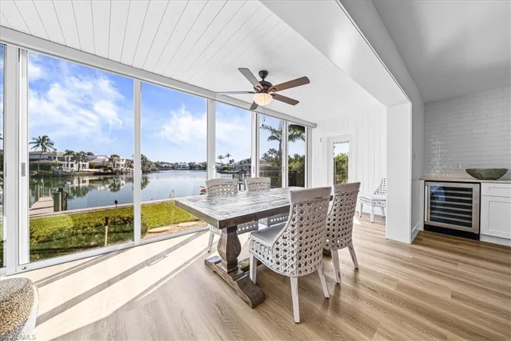 Sunroom / solarium featuring beverage cooler, wood finished floors, a water view, and bar