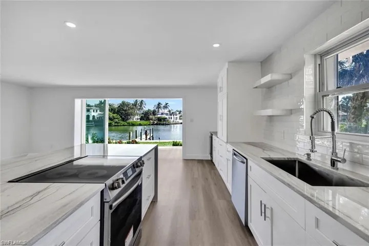 Kitchen with open shelves, stainless steel appliances, white cabinetry, light stone counters with waterfall, and recessed lighting