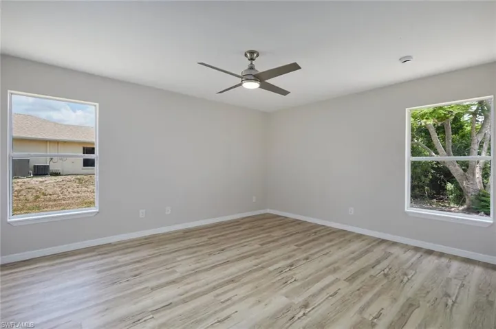 Empty room with light wood-style floors, ceiling fan, baseboards, and a smoke detector