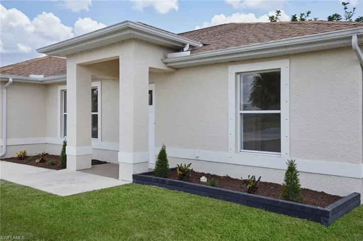 View of exterior entry featuring a shingled roof, stucco siding, and a lawn
