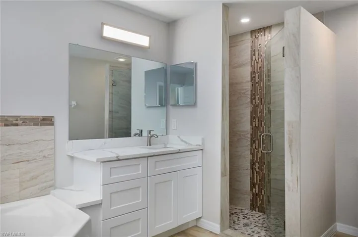 Full bath with a stall shower, a garden tub, vanity, baseboards, and recessed lighting