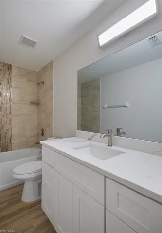 Bathroom with vanity, toilet, wood finished floors, and shower / washtub combination