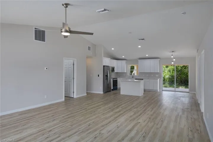 Unfurnished living room featuring baseboards, a ceiling fan, light wood-style floors, high vaulted ceiling, and recessed lighting