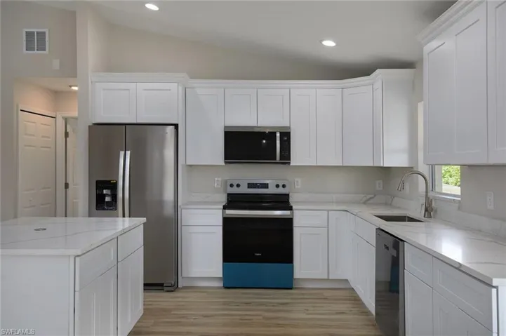 Kitchen with stainless steel appliances, vaulted ceiling, a sink, white cabinetry, and light wood-style flooring
