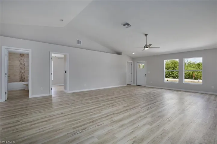 Unfurnished living room with a ceiling fan, lofted ceiling, light wood finished floors, and baseboards