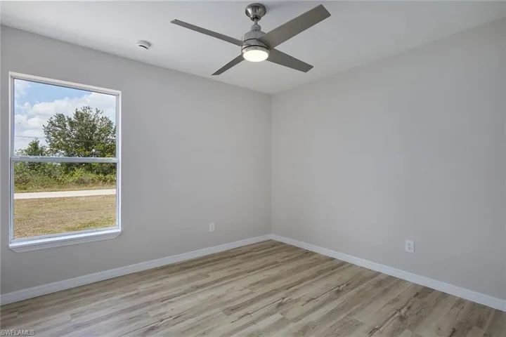 Unfurnished room featuring light wood finished floors, baseboards, a ceiling fan, and a smoke detector