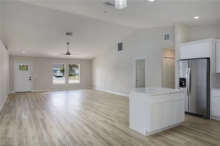Kitchen featuring stainless steel fridge, light wood-style floors, vaulted ceiling, white cabinets, and light countertops