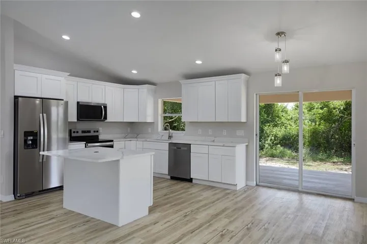 Kitchen with appliances with stainless steel finishes, light wood-type flooring, white cabinetry, recessed lighting, and lofted ceiling