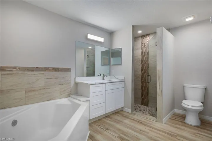 Full bath featuring a garden tub, a stall shower, vanity, toilet, and wood finished floors