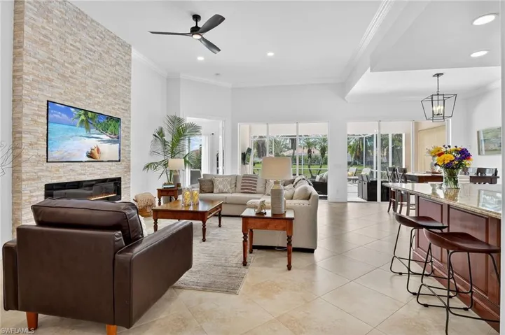 Great room featuring crown molding, a stone fireplace, ceiling fan, light tile patterned floors, and recessed lighting