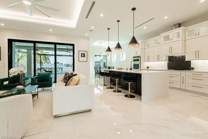 Kitchen with white cabinetry, tasteful backsplash, a kitchen breakfast bar, an island with sink, and pendant lighting