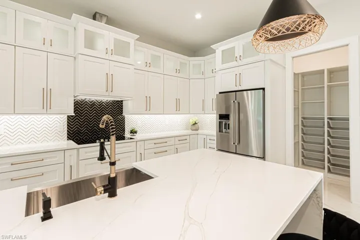 Kitchen with white cabinetry, tasteful backsplash, light stone countertops, decorative light fixtures, and high end refrigerator