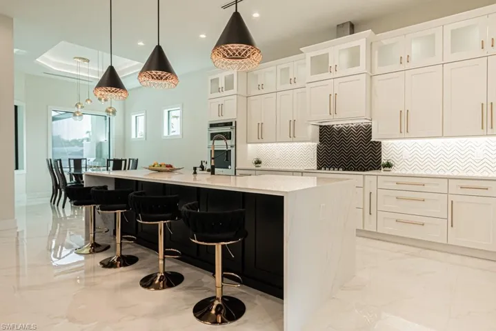 Kitchen with a breakfast bar, white cabinets, stainless steel double oven, hanging light fixtures, and a center island with sink