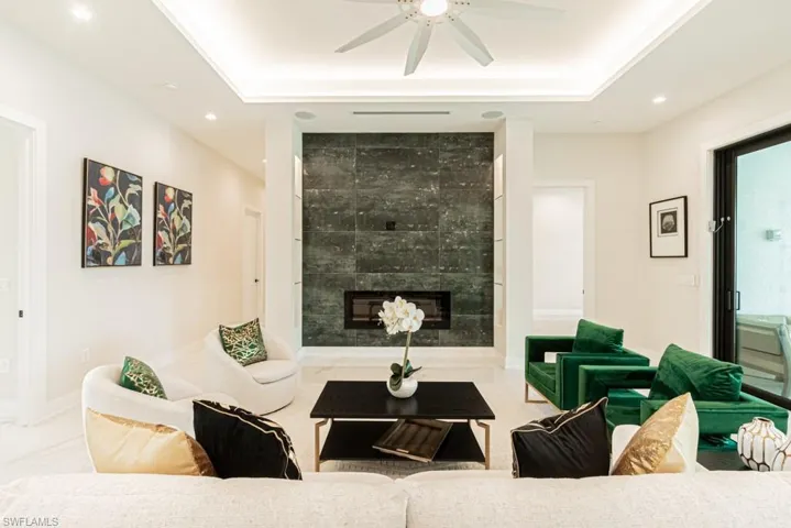 Living room featuring ceiling fan, a large fireplace, and a raised ceiling