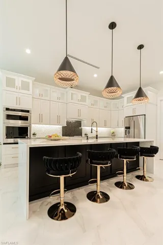 Kitchen with hanging light fixtures, a kitchen breakfast bar, white cabinets, and appliances with stainless steel finishes