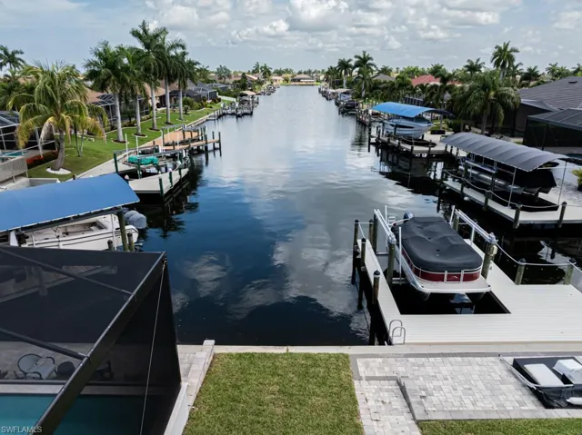 View of dock featuring a water view, a lanai, and a lawn