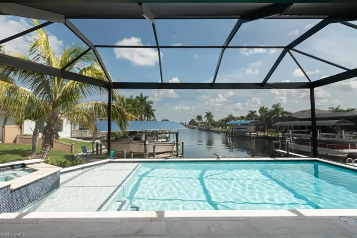 View of swimming pool with a water view, an in ground hot tub, glass enclosure, and a boat dock