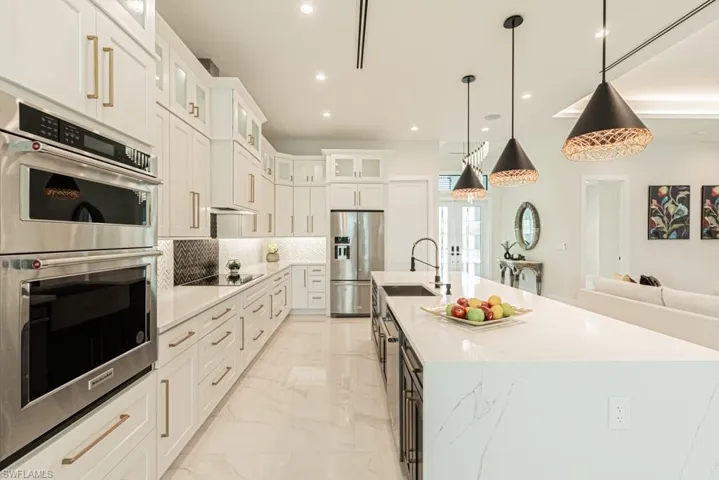 Kitchen with white cabinets, decorative backsplash, hanging light fixtures, a large island, and stainless steel appliances