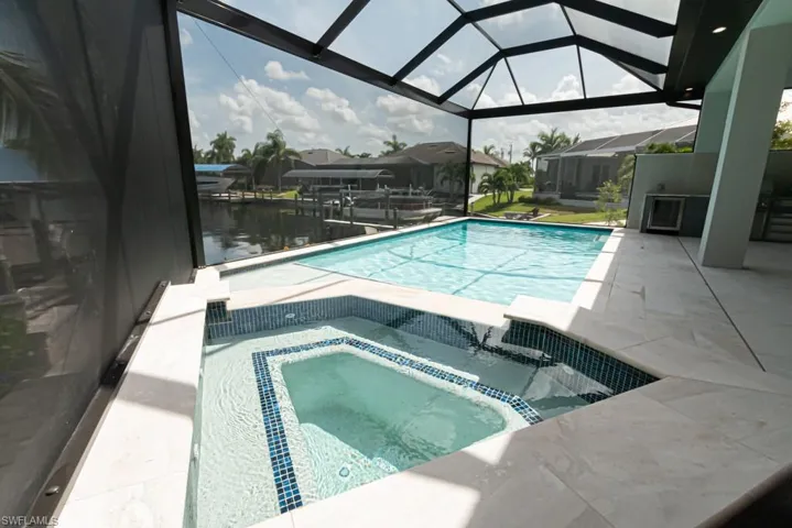 View of pool with an in ground hot tub, a water view, glass enclosure, and a patio area