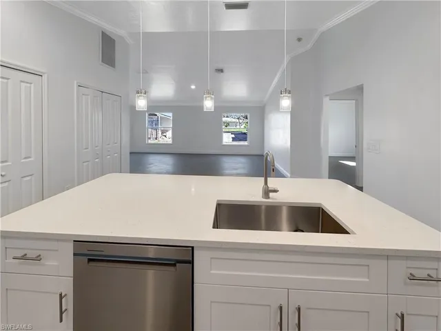 Kitchen featuring white cabinetry, stainless steel dishwasher, light stone countertops, ornamental molding, and hanging light fixtures