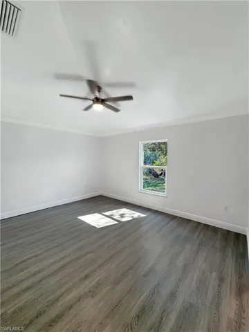 Spare room with dark wood-style flooring, ceiling fan, and crown molding