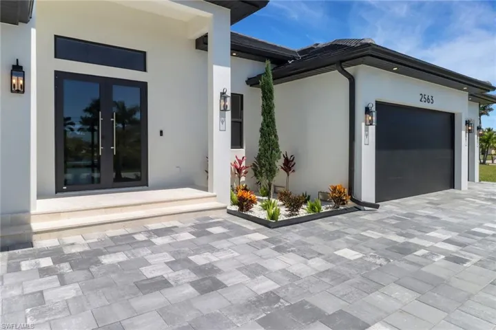 Property entrance featuring decorative driveway, and lush landscape garden
