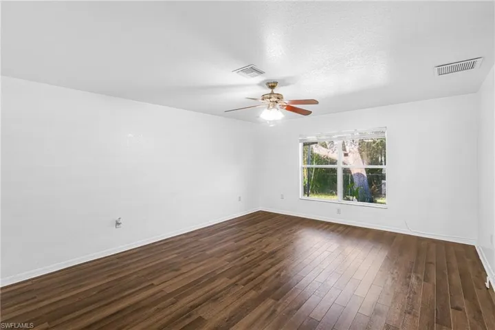 Room featuring wood-finish flooring, a ceiling fan with integrated lighting, and a large window with natural light
