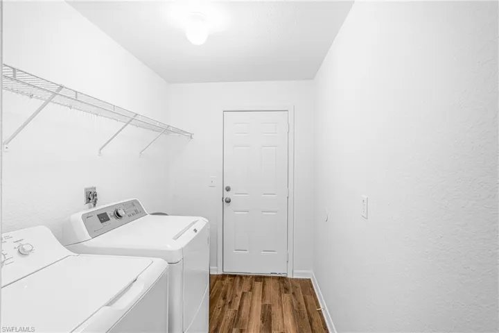 Dedicated laundry area with wood-finish flooring, white walls, overhead lighting, and a wire shelving system