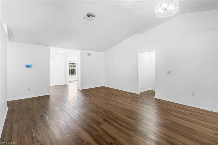 Spacious room featuring wood-finish flooring, vaulted ceilings, and a modern ceiling light fixture