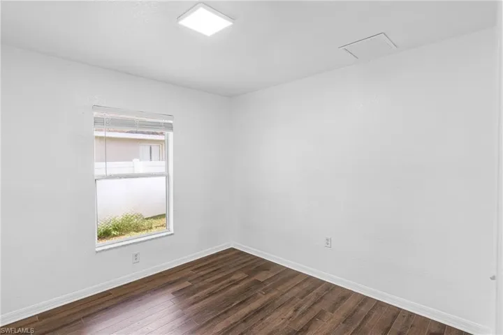 Room featuring wood-finish flooring, white painted walls, and a single window with horizontal blinds